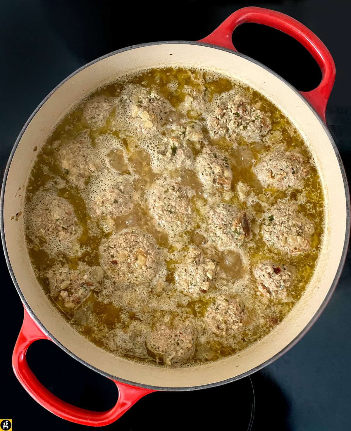 Hilopites pasta and grated parmesan added to meatball soup in a Dutch oven.