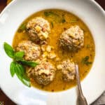 Lemony meatball soup with hilopites pasta and fresh basil in a white bowl with a spoon.