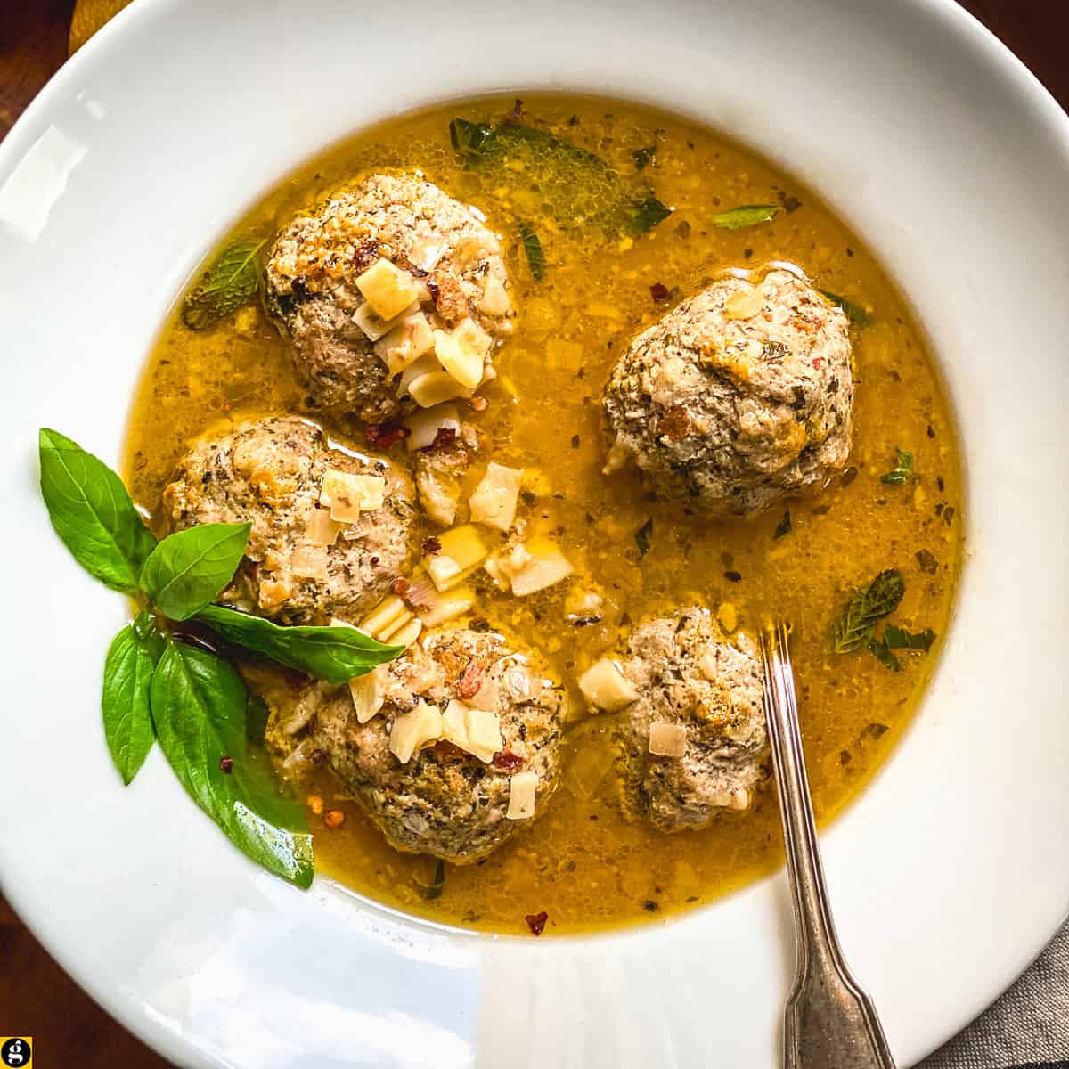 Lemony meatball soup with hilopites pasta and fresh basil in a white bowl with a spoon.