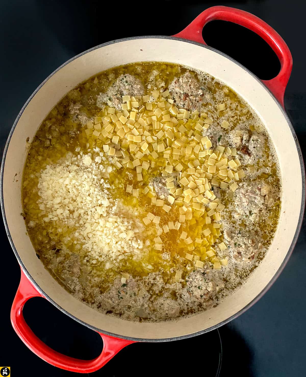 Meatballs simmering in chicken broth in a red Dutch oven.