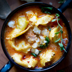 A bowl with chicken tortellini soup on a wooden surface.