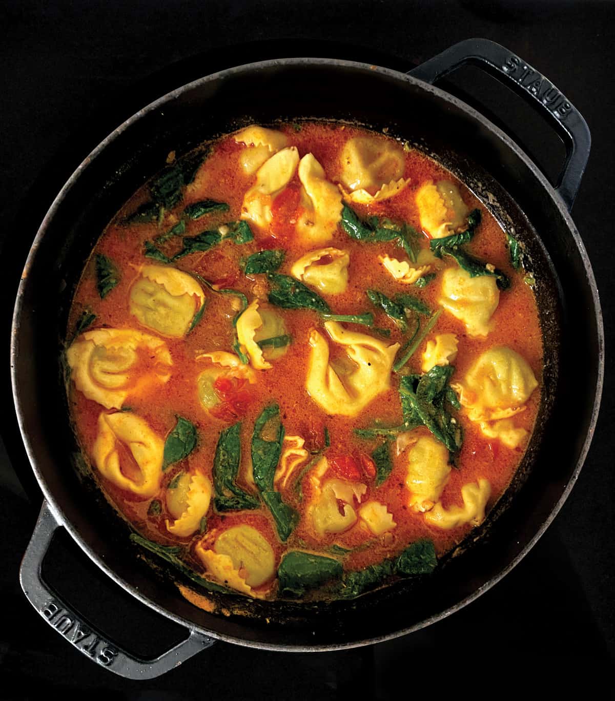 Tortellini pasta and spinach in a tomato broth in a stockpot.