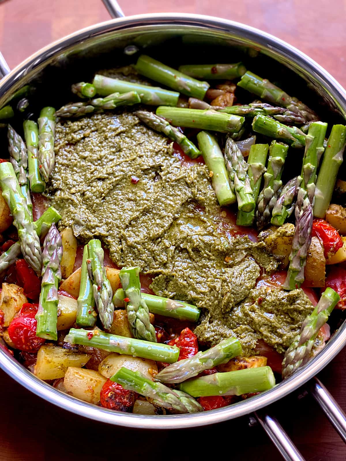 A salmon fillet covered with pesto sauce surrounded with cherry tomatoes, potatoes and asparagus in a baking pan.