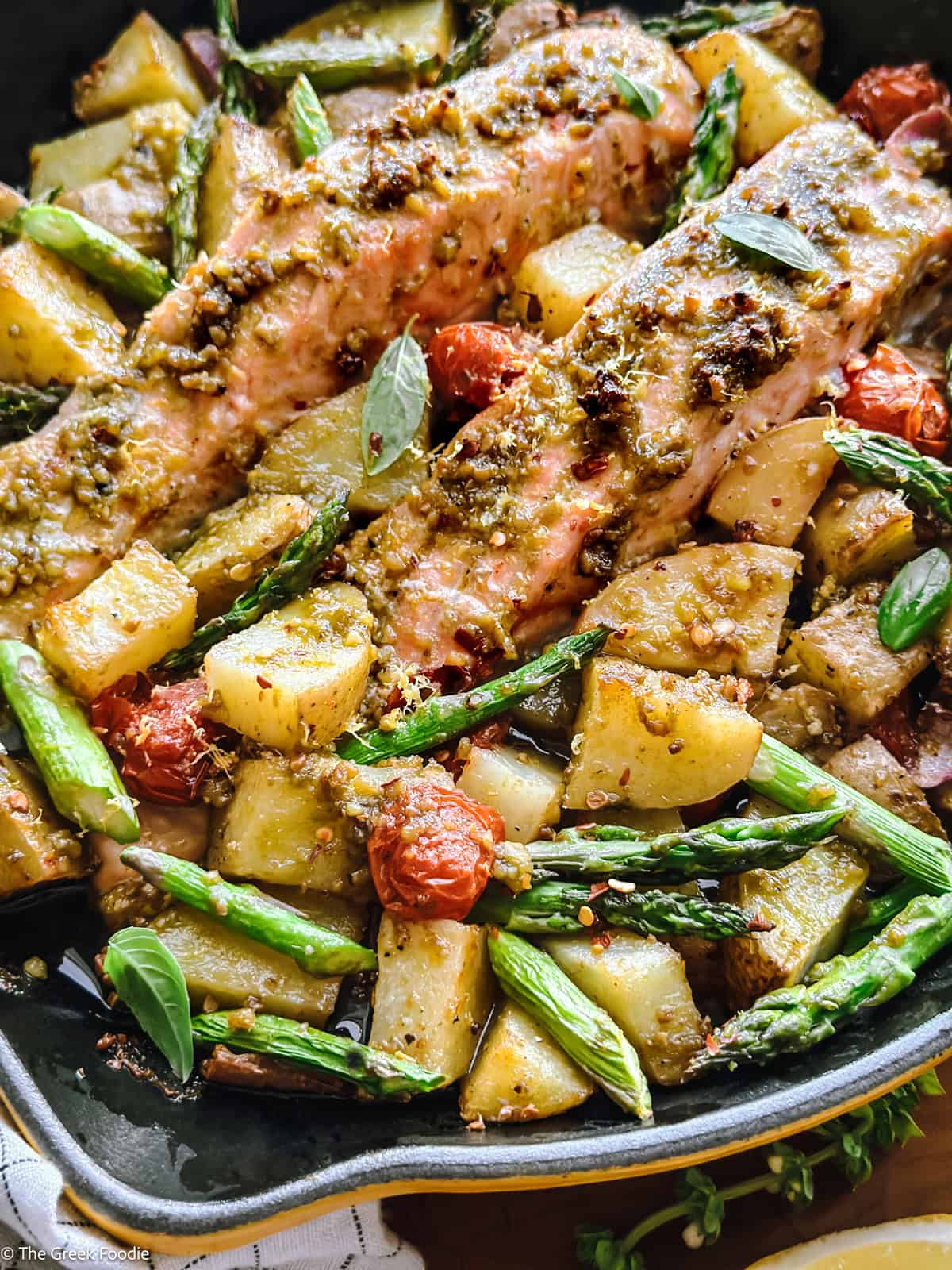 Greek salmon recipe with pesto, cherry tomatoes, and asparagus in a skillet