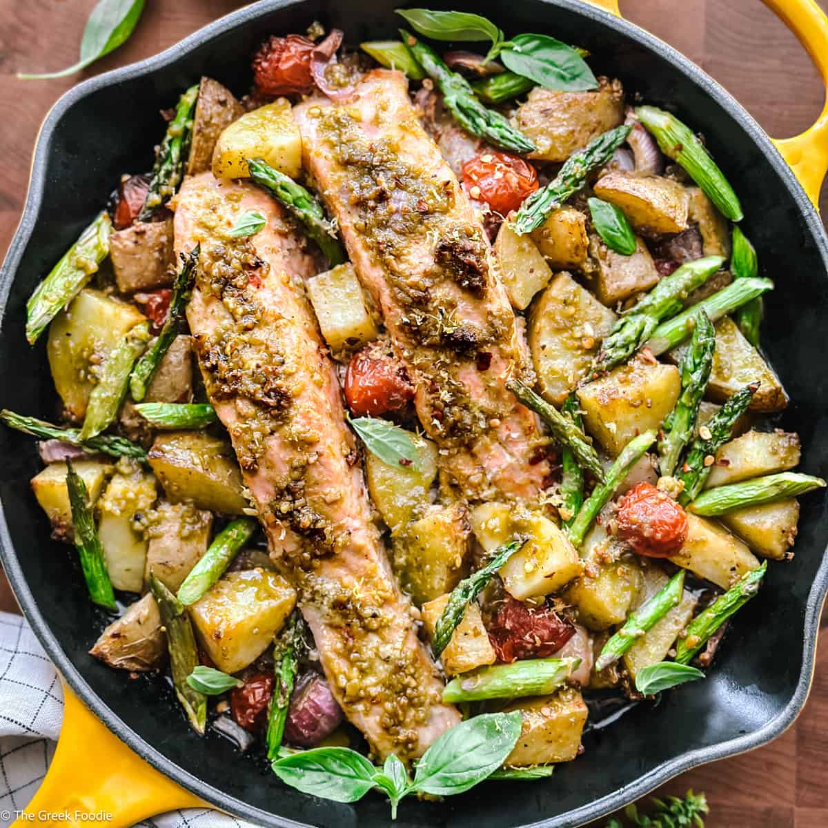 Greek salmon recipe with pesto, cherry tomatoes, and asparagus in a skillet