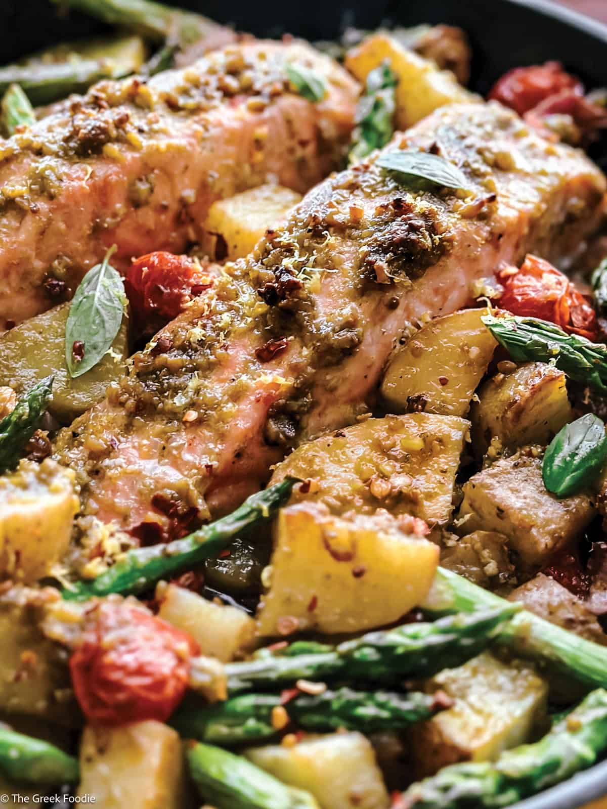 Close up of Greek salmon fillets with pesto, cherry tomatoes, and asparagus in a skillet