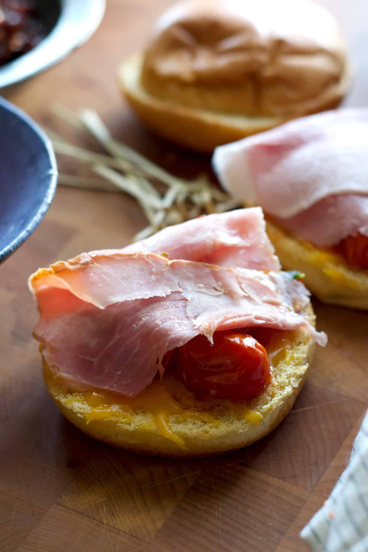 A half of a brioche bun with some tomato and a slice of ham on a table.