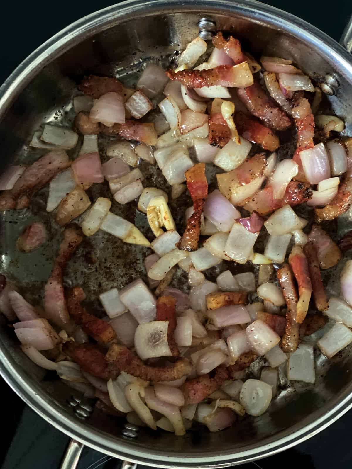 Guinciale pieces in a deep sauce pan with chopped onion and garlic.