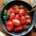 A black bowl with tomato confit, herbs and a spoon.