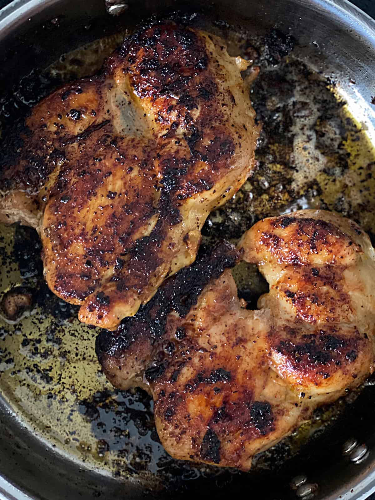 Two chicken thighs cooking in a large sauce pan.