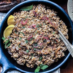 A serving bowl with lentils with rice two lemon wedges and utensils.