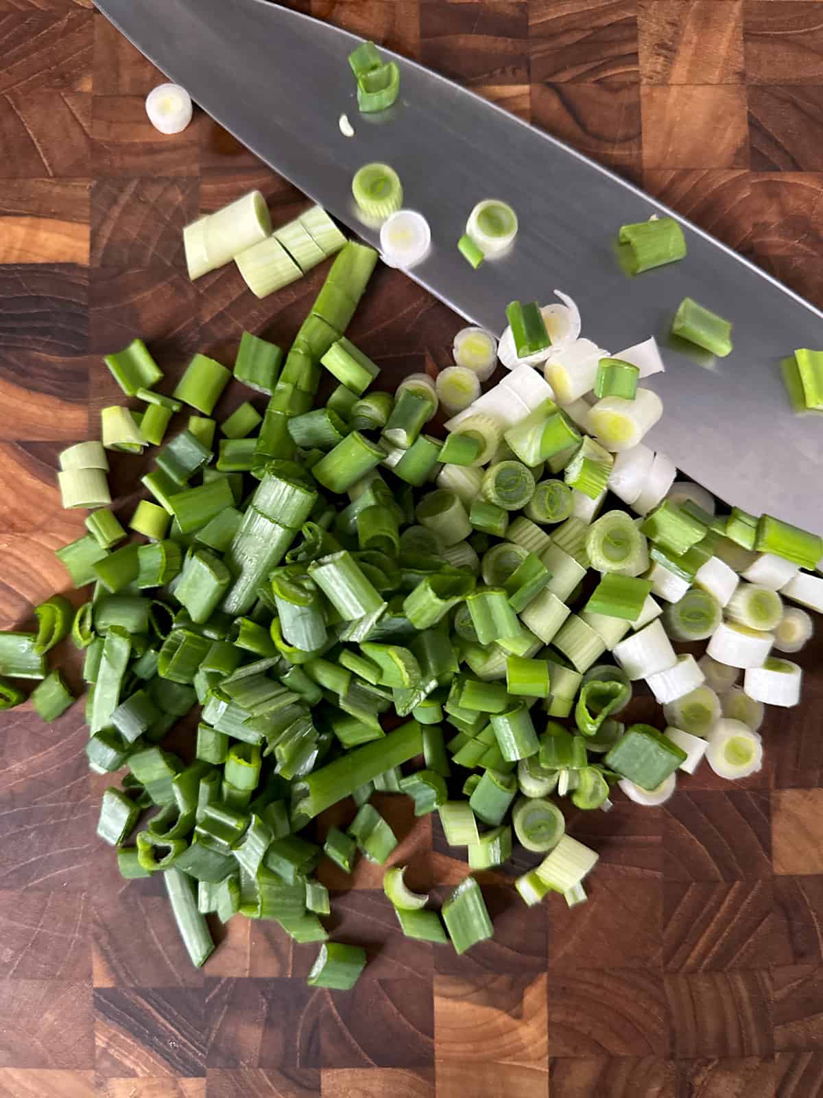 Chopped scallions and a chef's knife on a butcher block.