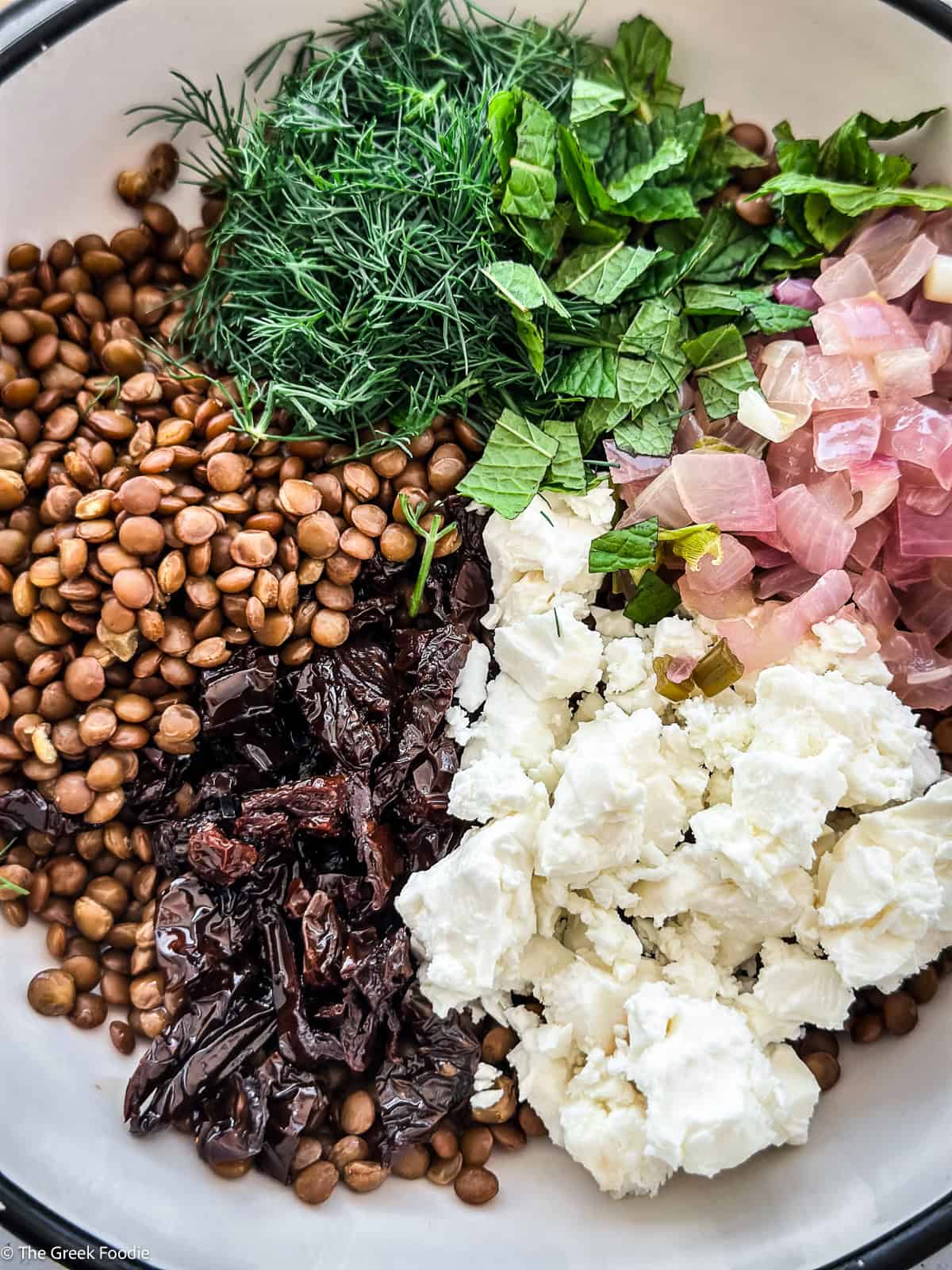 Lentils, sun-dried tomatoes, feta and herbs being tossed in a large bowl