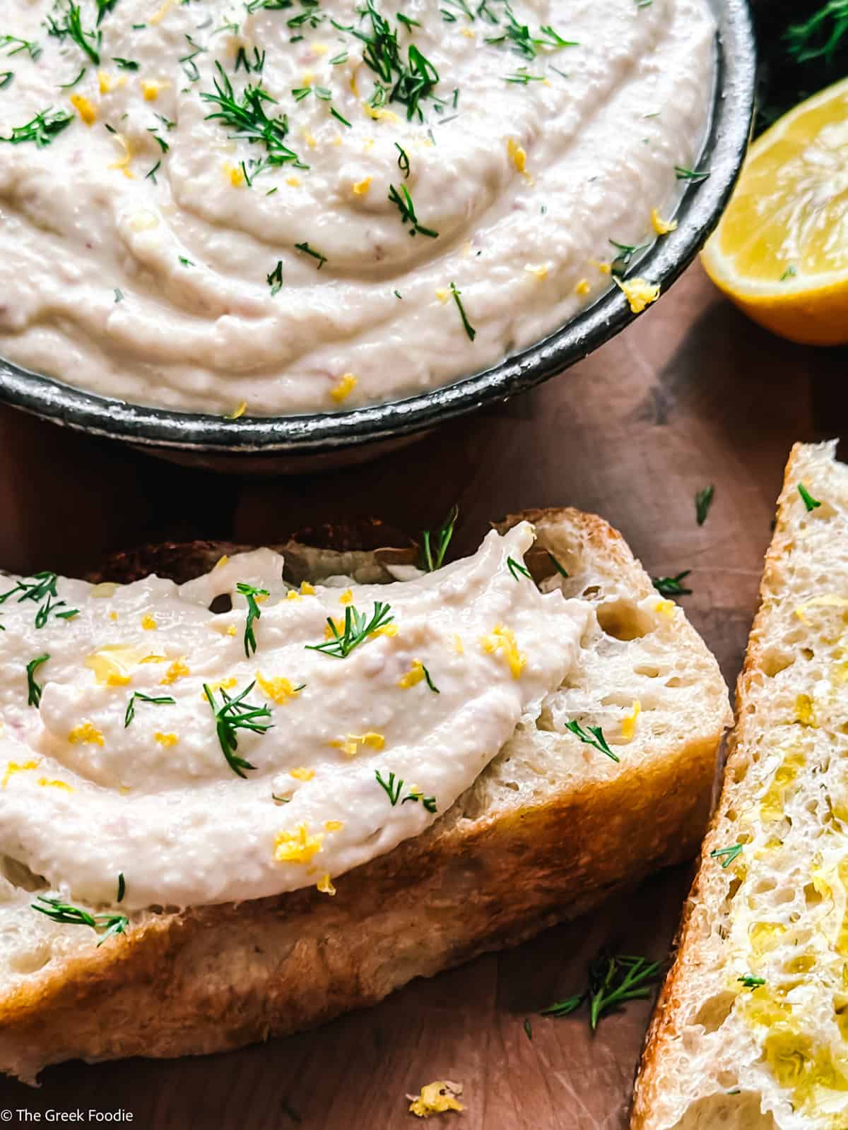 A bowl of taramosalata with bread slices and lemon halves on the side