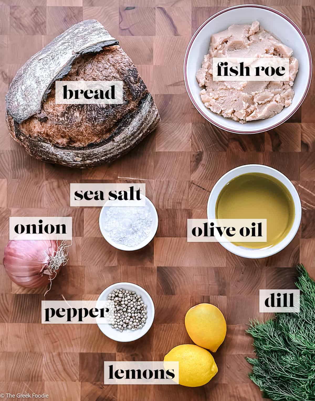 Ingredients for taramosalata on a wooden surface: tarama fish roe, lemon, onion, bread, and olive oil