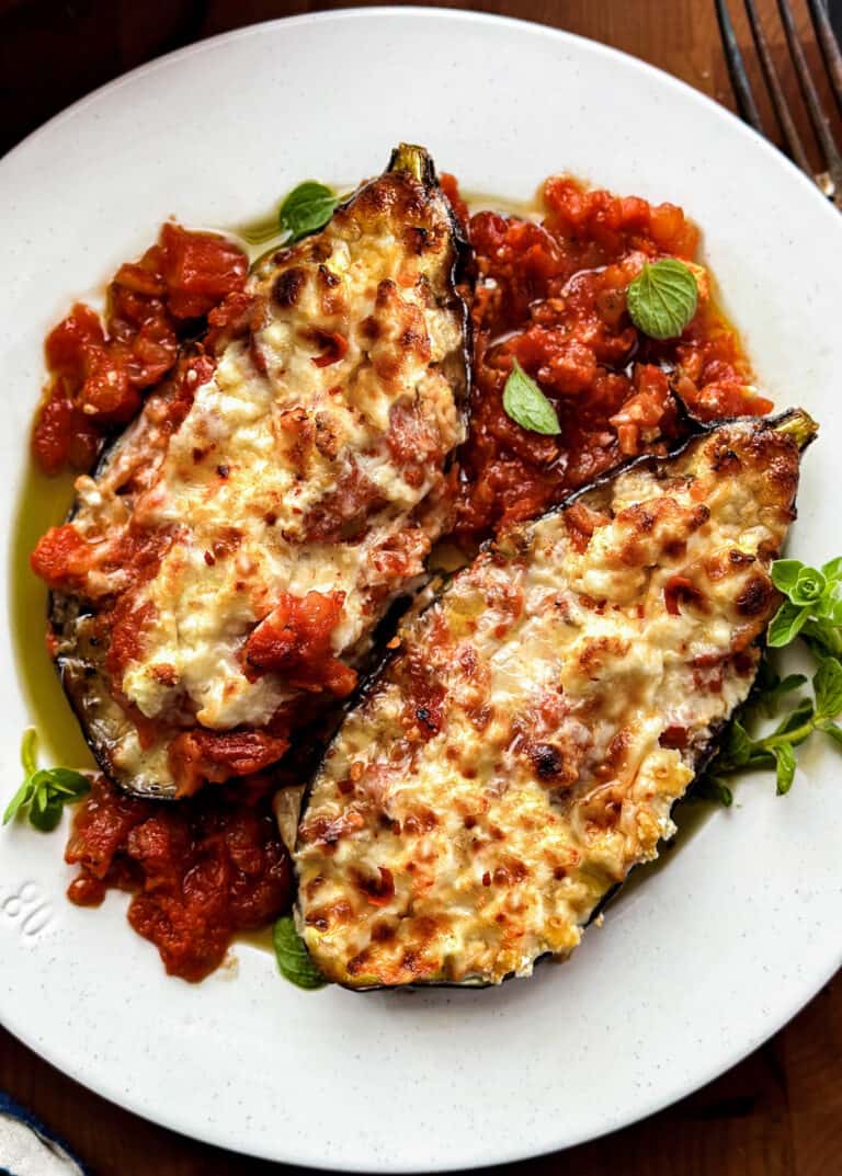 A plate with two eggplant papoutsakia on a wooden table.