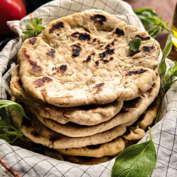 A stack of Greek pita bead wrapped in a cloth napkin with some herbs.