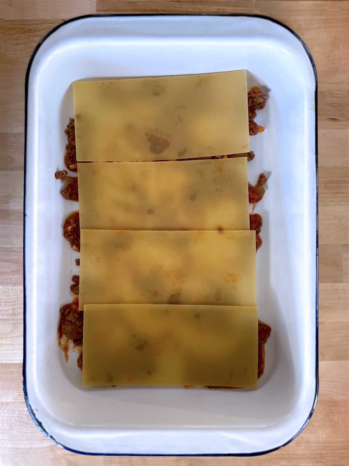 A baking pan lined with meat sauce and lasagna sheets.