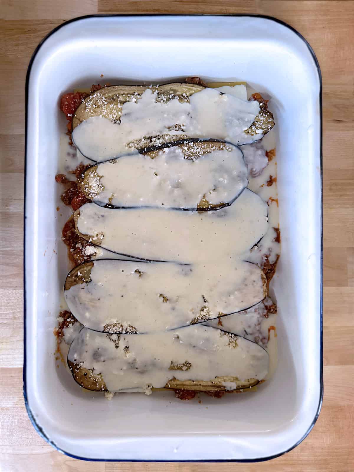 A baking pan lined with meat sauce, eggplant slices and béchamel.