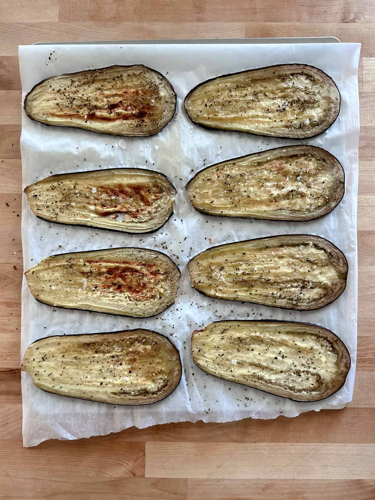 A baking sheet lined with parchment paper and cooked eggplant slices.