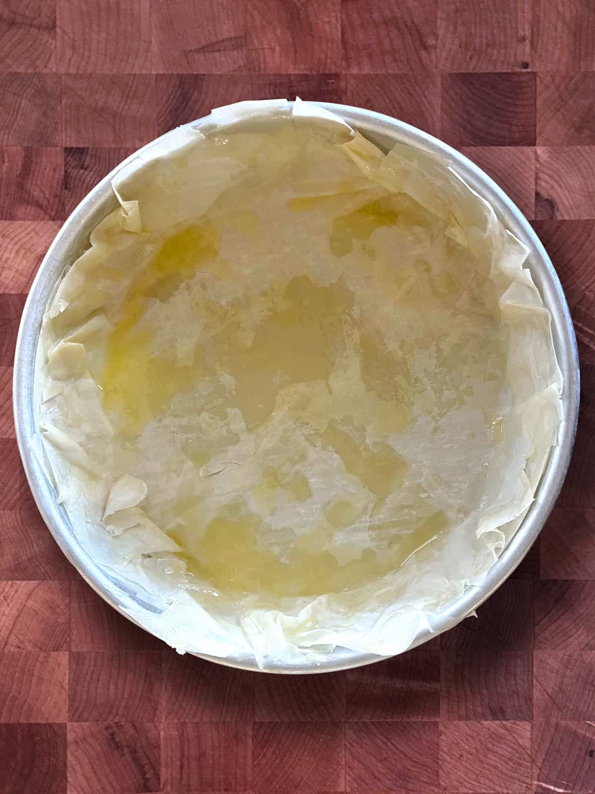 A round aluminum pan lined with buttered phyllo sheets.