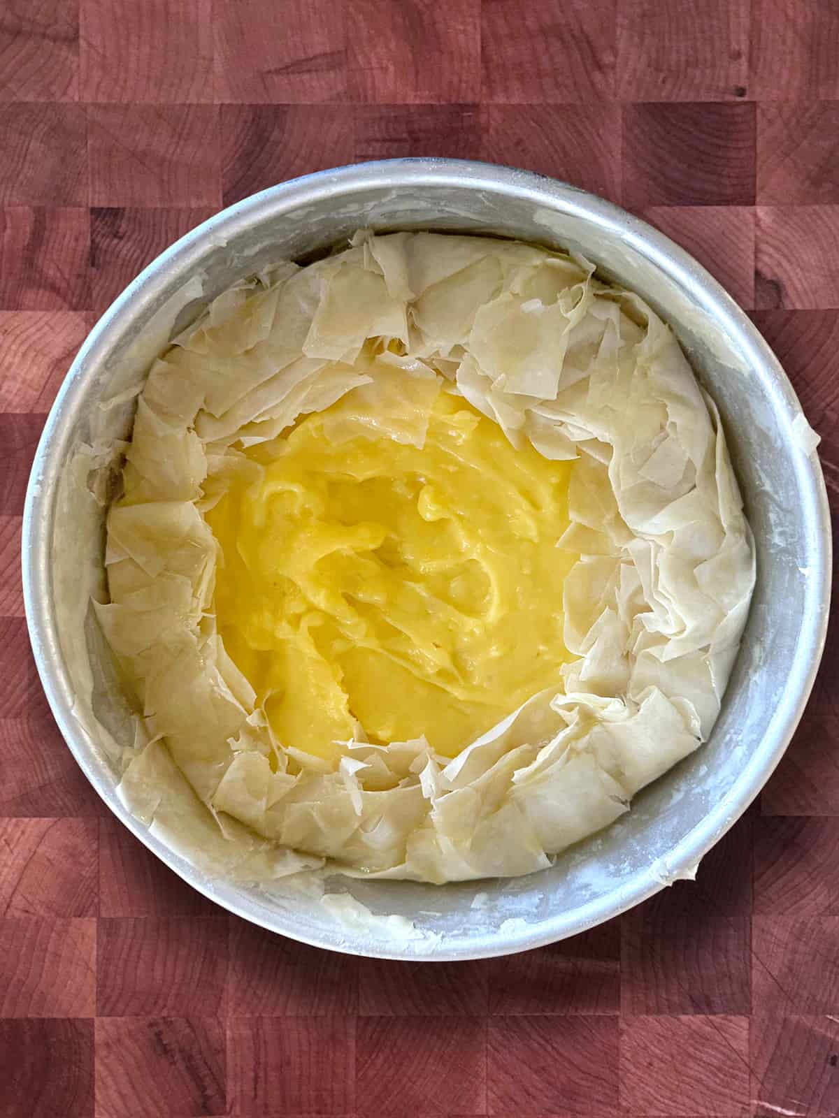 A round aluminum pan lined with buttered phyllo sheets folded over custard.