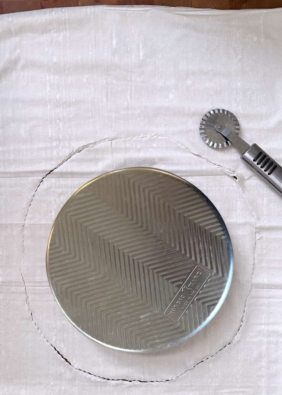 Phyllo sheets with a circle line traced with a pastry cutter, and an aluminum pan in the middle of the circle.