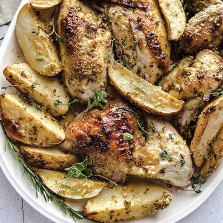 A platter with roasted Greek lemon chicken pieces and lemon potatoes.