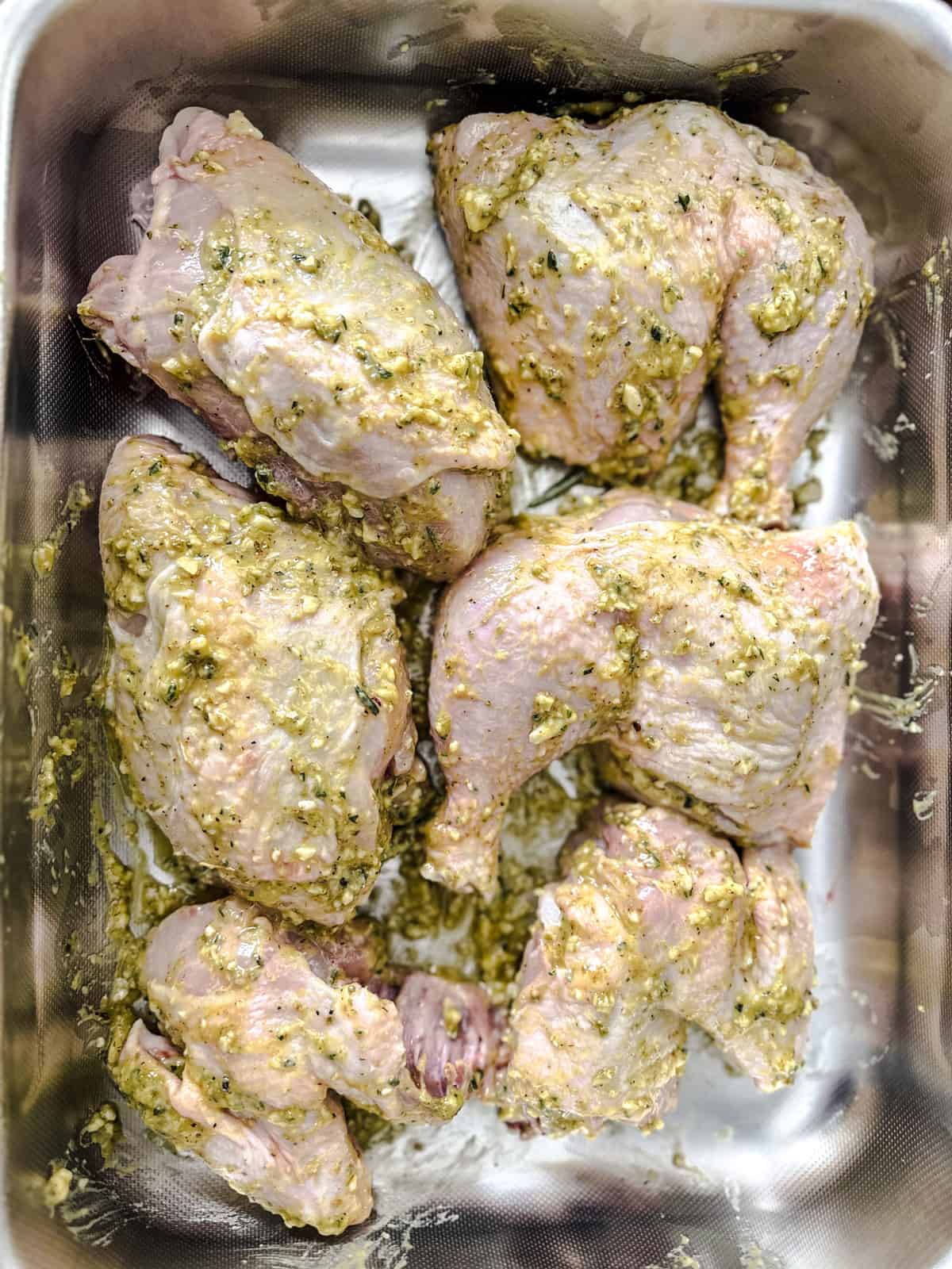 Chicken pieces rubbed with marinade in a baking pan.