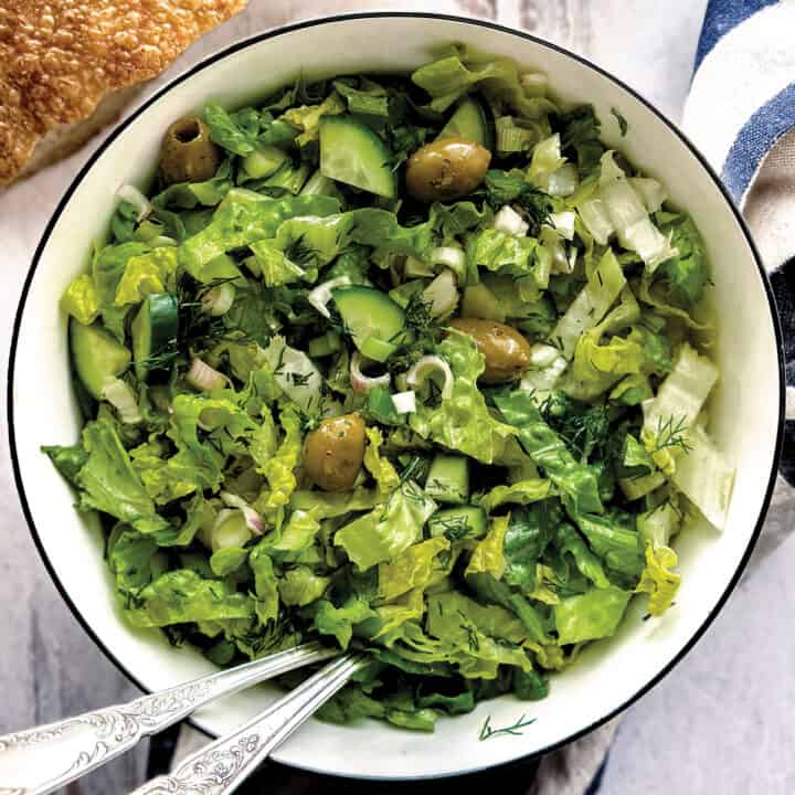 A bowl with Greek lettuce salad maroulosalata and two serving utensils.