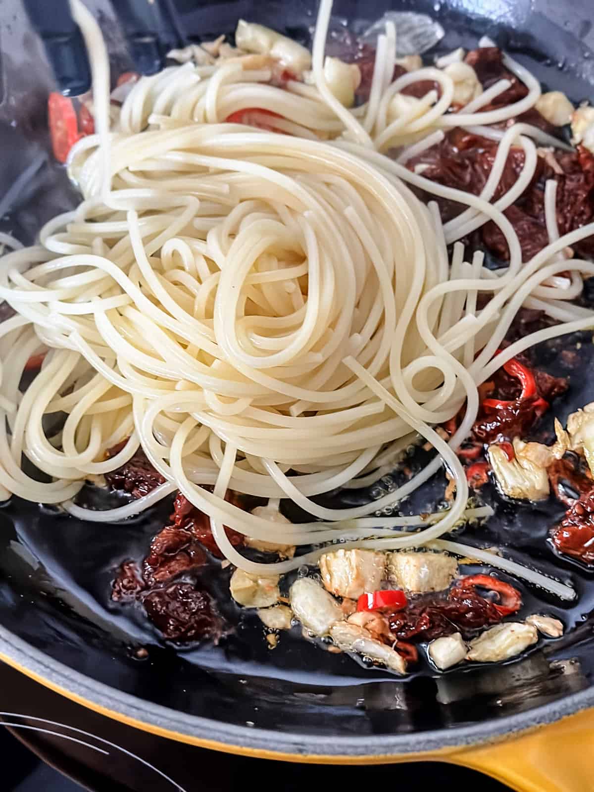 Cooked spaghetti transferring to a skillet with garlic and chili pepper.