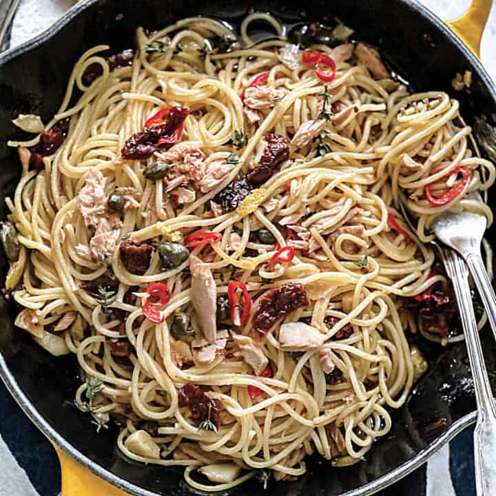 A cast iron skillet with Mediterranean tuna spaghetti and utensils.