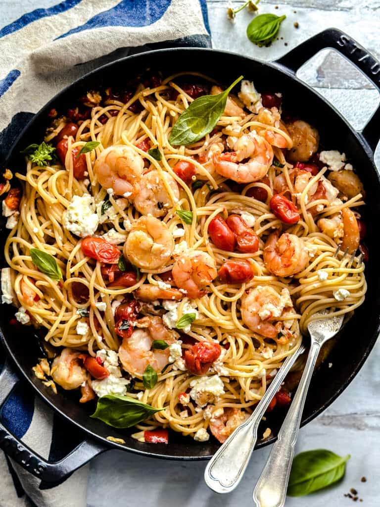 A cast iron large saucepan with spicy shrimp spaghetti - garidomakaronada, utensils, and a cloth napkin.