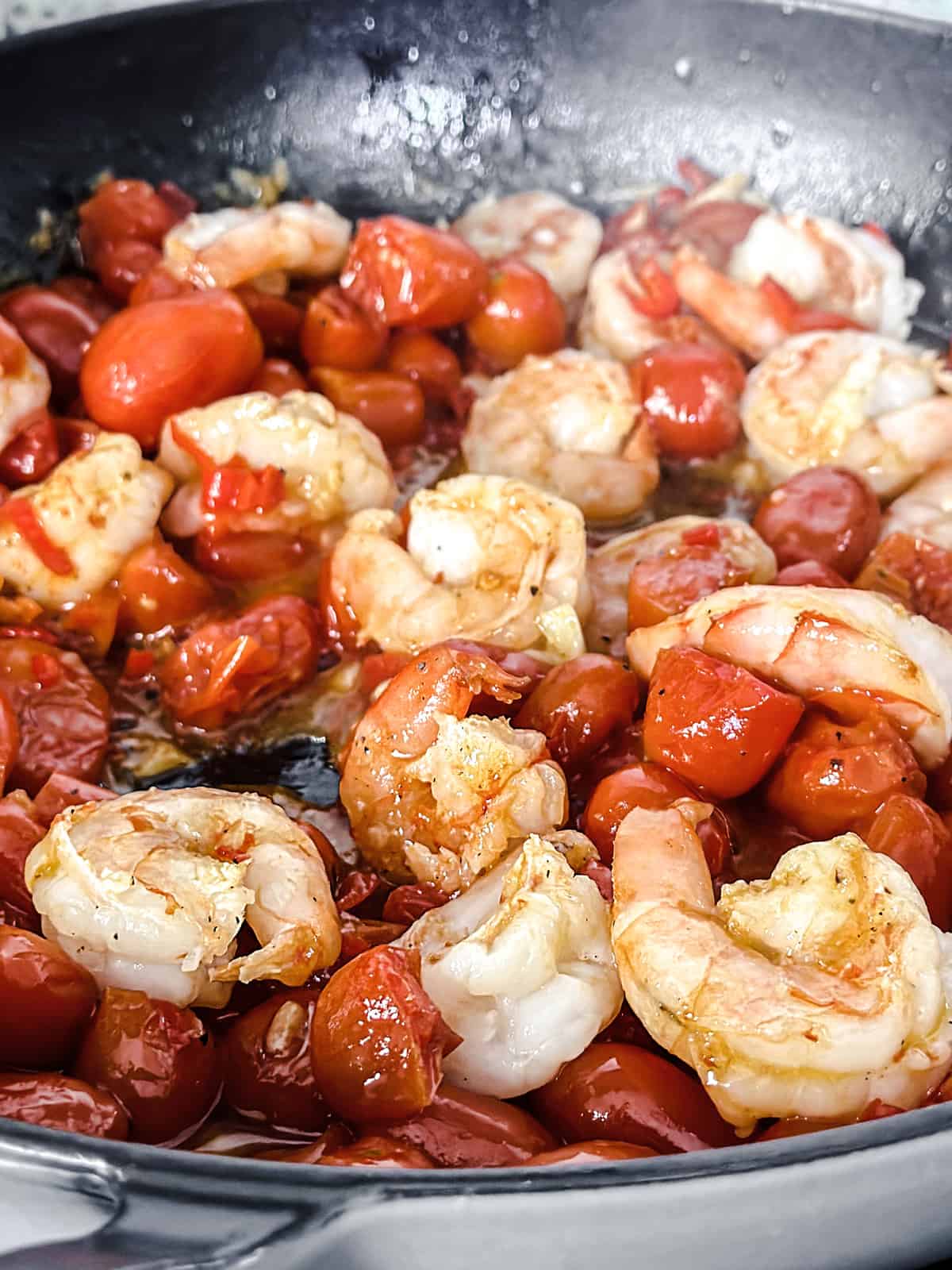 Cherry tomatoes, shrimp, chopped garlic and chili peppers in olive oil in a large deep sauté pan.
