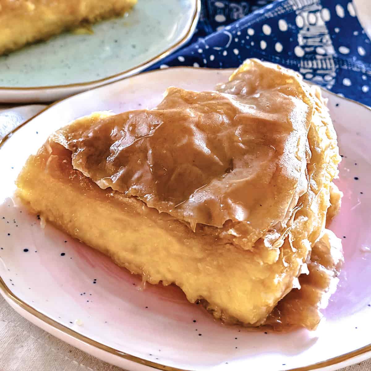 Two pieces of galaktoboureko on plates on top of a cloth napkin