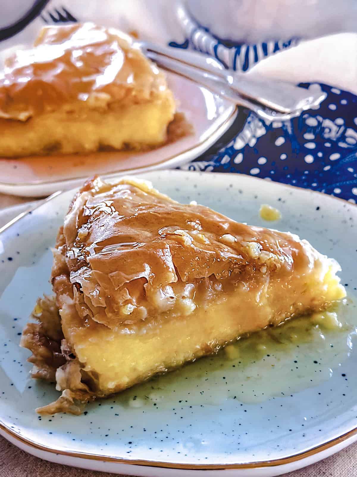 Two pieces of galaktoboureko on plates on top of a cloth napkin, behind them an aluminum pan