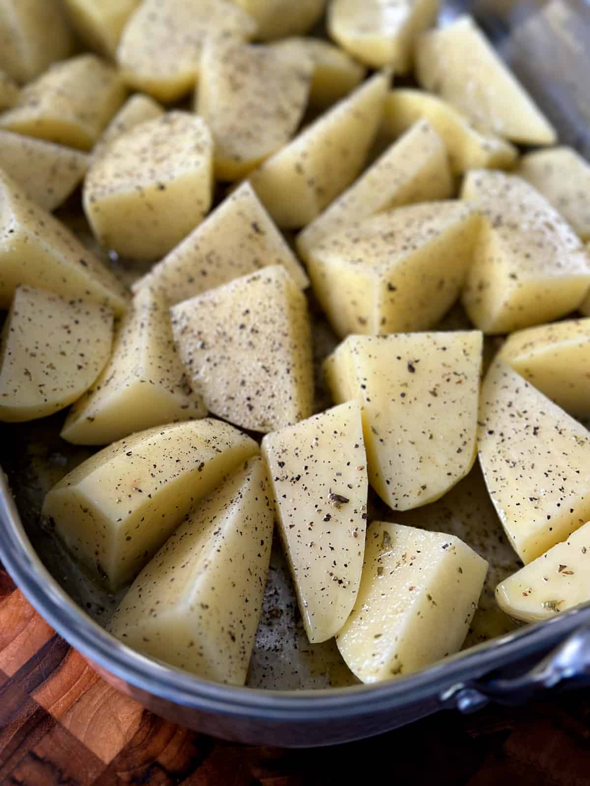A baking pan with potatoes seasoned with oregano, salt and pepper on a cutting board.