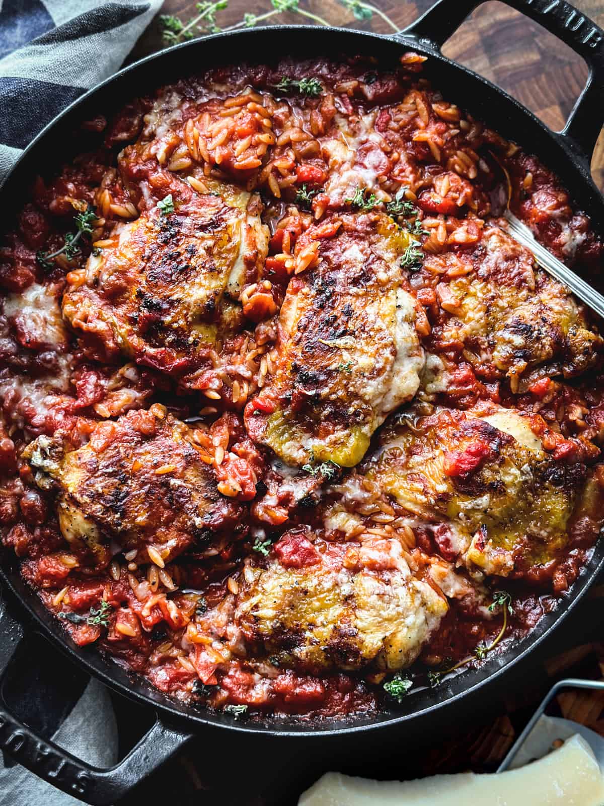 A large cast iron deep skillet with Greek chicken orzo-Giouvetsi and a spoon, on a cloth napkin.