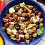 Close up of a shallow bowl with marinated olives in olive oil, lemon peel, feta cheese, and herbs.