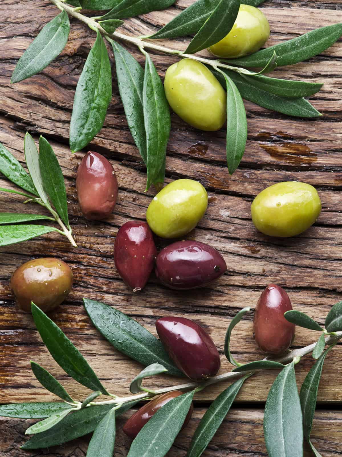 Ten olives of different colors and sizes with olive tree branches on a old wooden table.