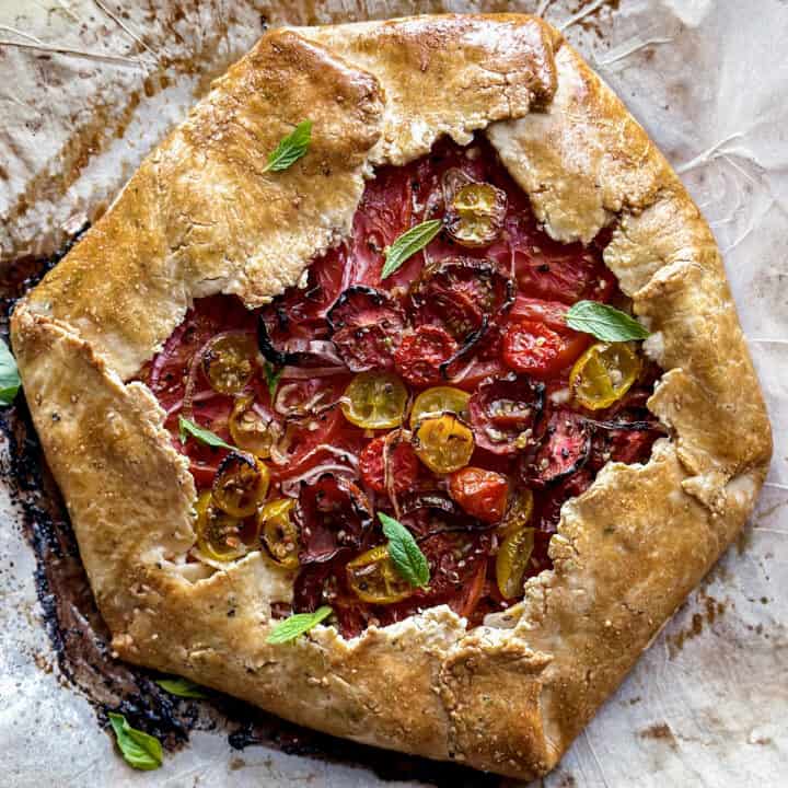 A tomato galette with feta cheese, onions and tomatoes on parchment paper.