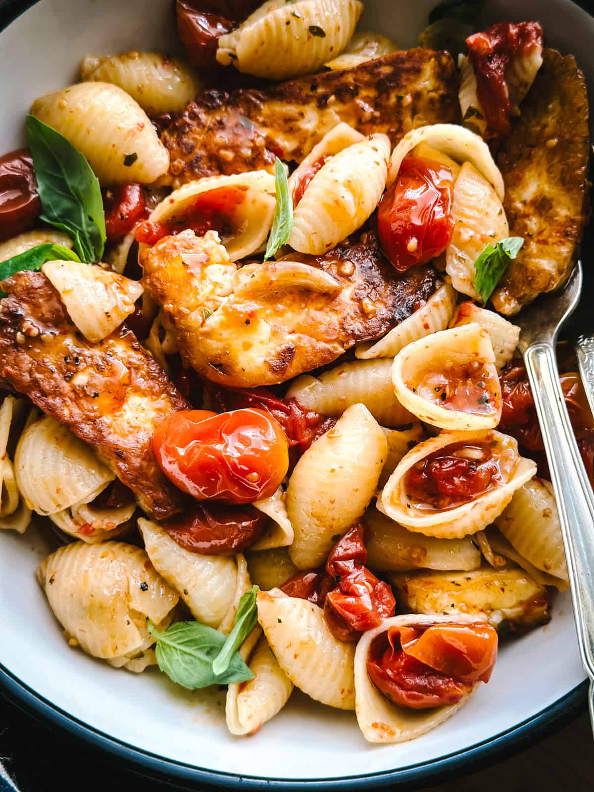 A bowl with burst tomato pasta with fried halloumi and a spoon.