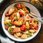 A bowl with burst tomato pasta with fried halloumi and a spoon.