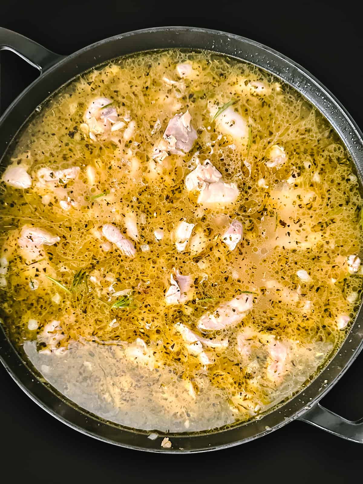 A large deep skillet with broth, beans and chicken pieces.