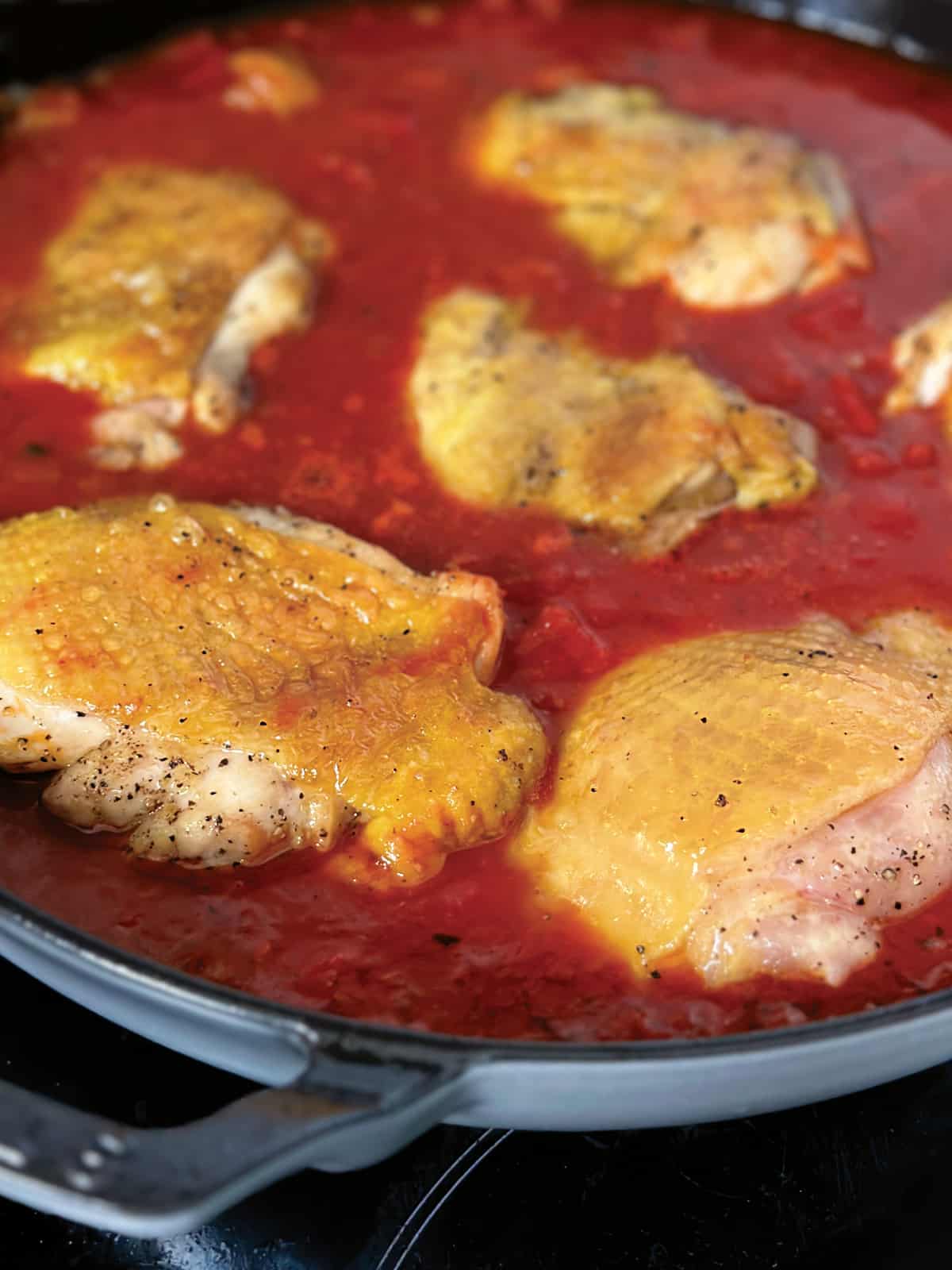 Chicken thighs, and tomato sauce in a skillet.