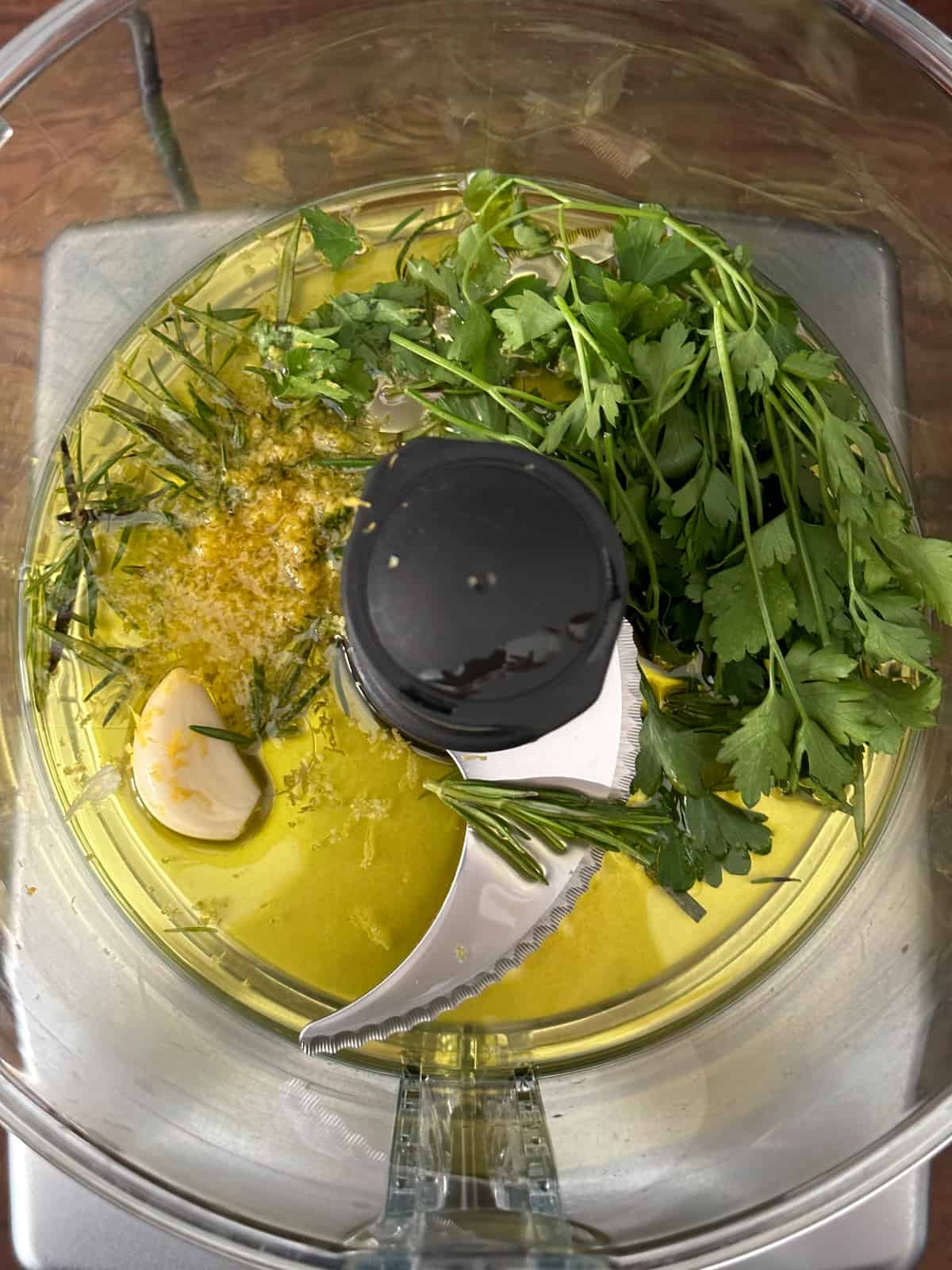  Aclove of garlic, parsley and romesy leaves, mustard and olive oil in  a food processor bowl.