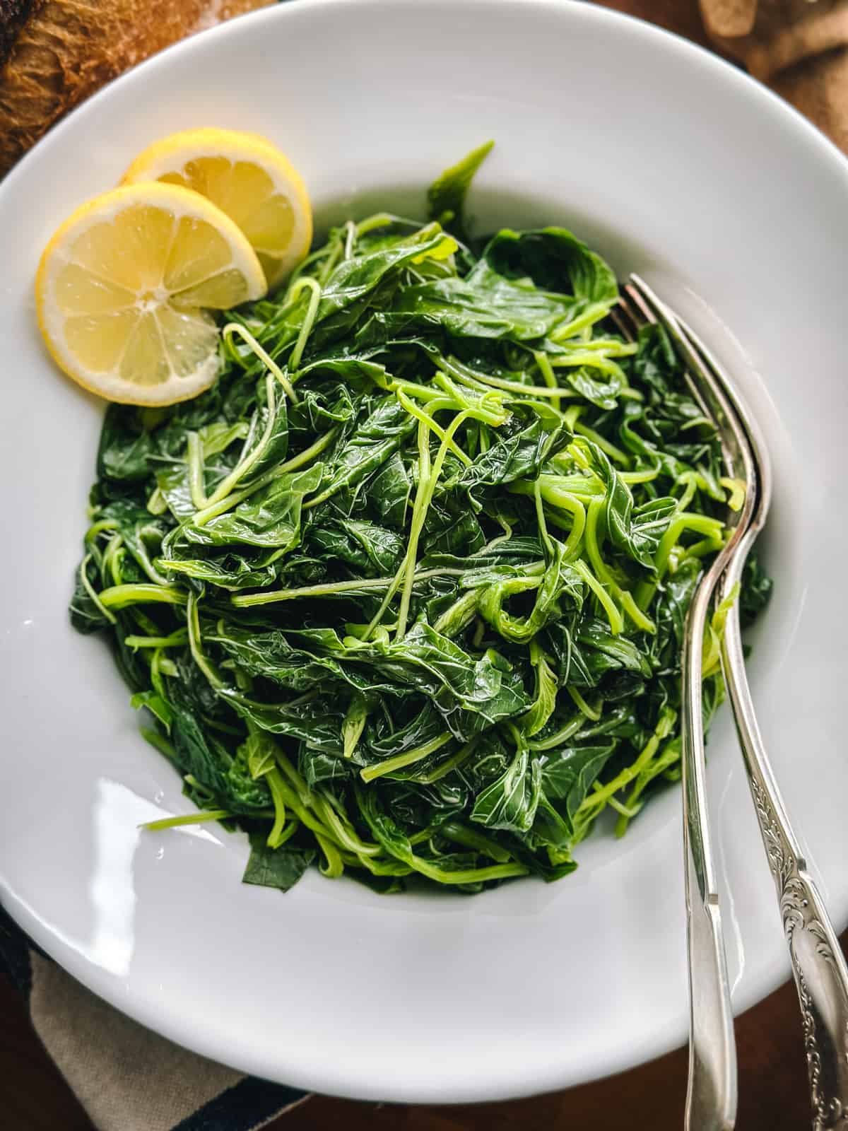 A late with horta rasta-Greek greens wit two slices of lemon and utensils.