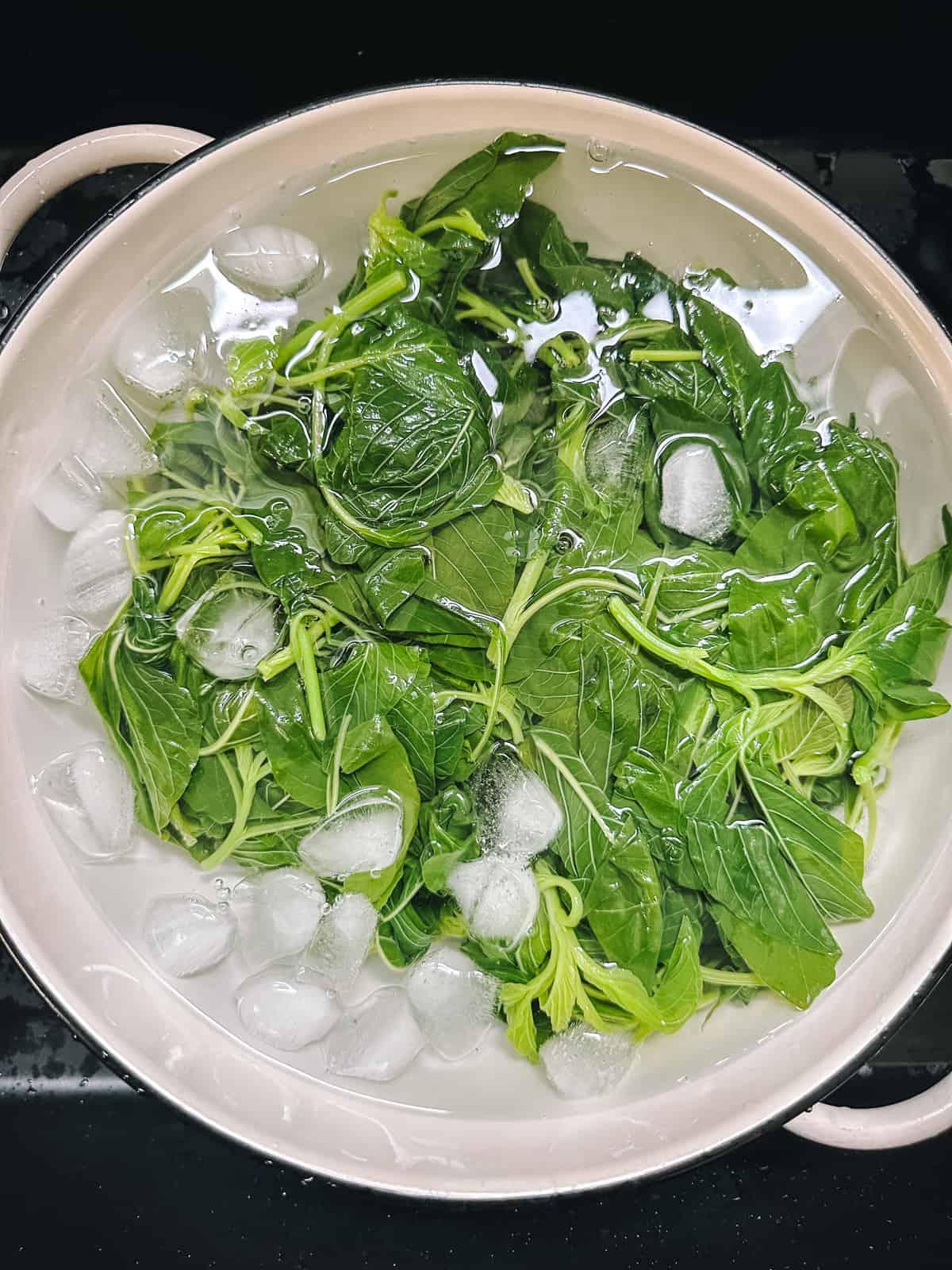 Cooked greens in a large pot filled with water and ice cubes.