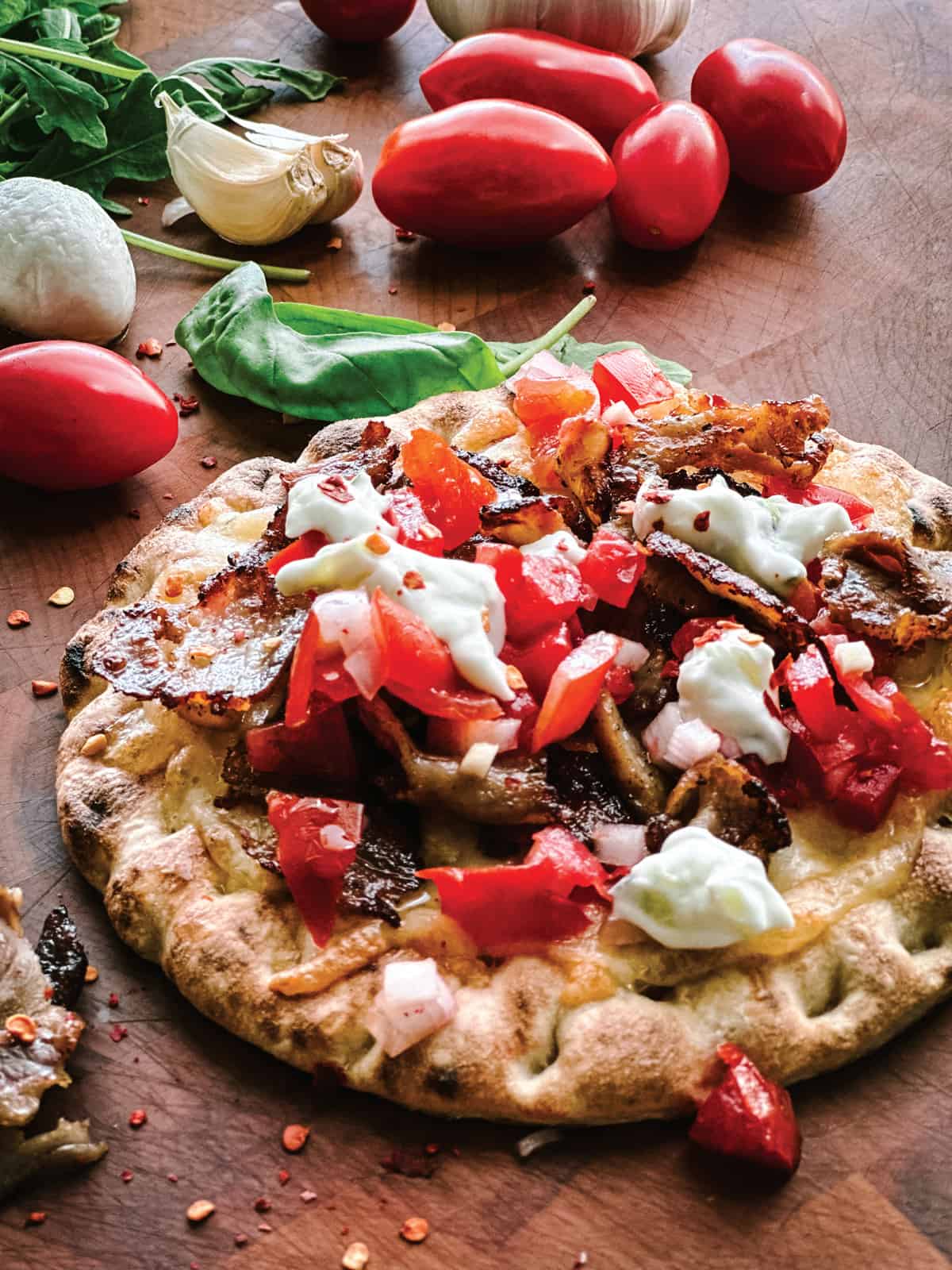 A pita pizza with gyro, tomatoes and tzatziki sauce.