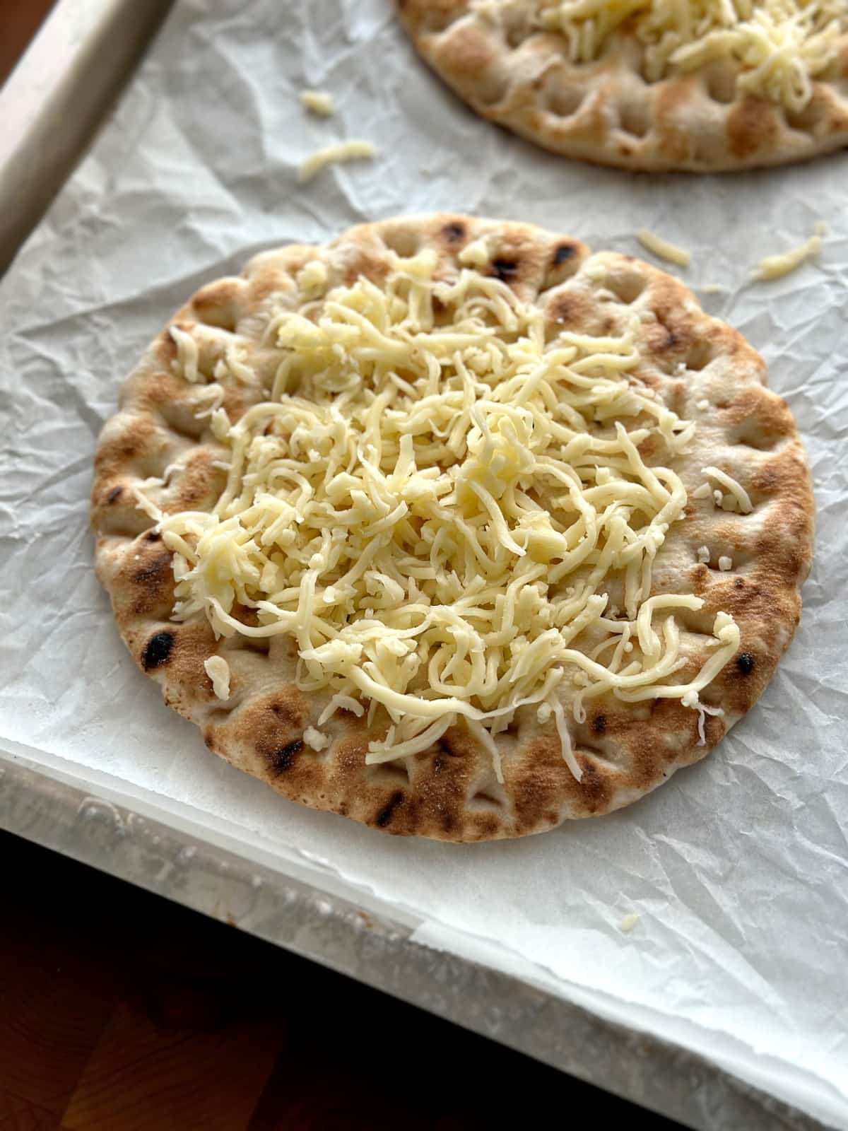 A pita loaded with cheese on parchment paper.